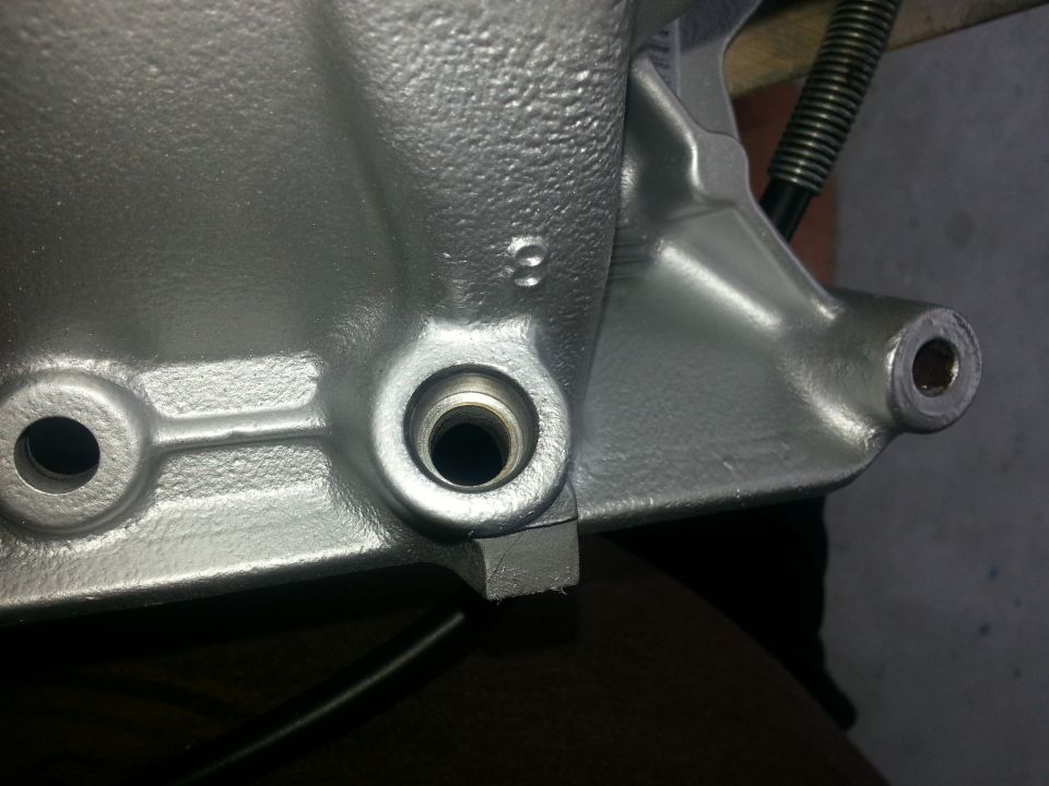Close-up of a cast metal engine component with two bolt holes and a threaded opening