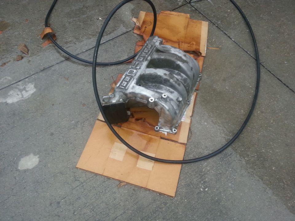 Aluminum engine intake manifold on cardboard, with black hose