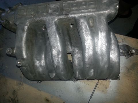 1994 Ford Bronco - Aluminum intake manifold with runners and mounting holes, a wrench is attached.