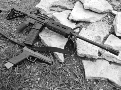 1996 Ford Bronco - An assault rifle and a handgun are placed on the ground amidst grass and rocks.