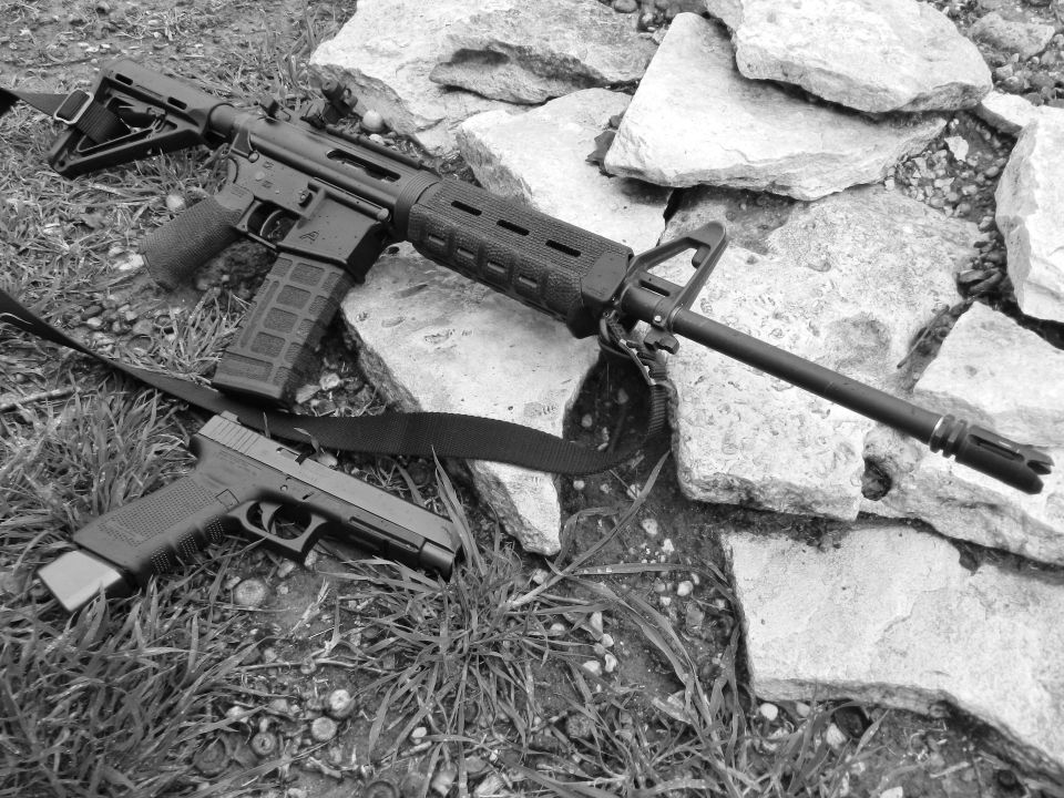 Assault rifle and handgun on grass and rocks