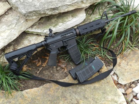 1996 Ford Bronco - A black assault rifle with two magazines and a sling is displayed on a rocky and grassy surface.
