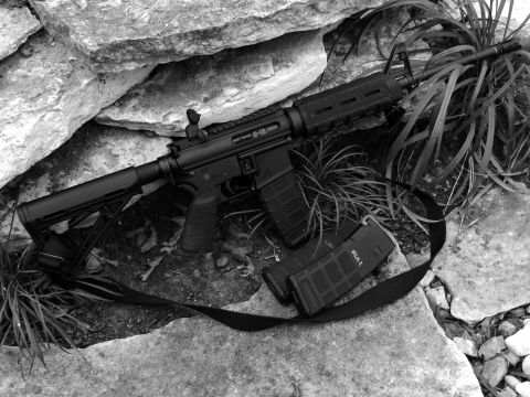 1996 Ford Bronco - An assault rifle and two magazines are placed on rocks with grass growing around them.