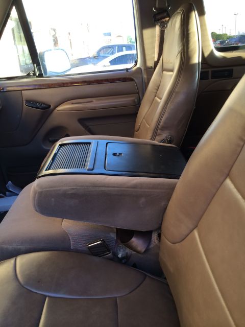 1996 Ford Bronco - The interior of a vehicle features tan cloth and leather seats with a prominent center console and armrest.
