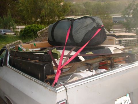 1973 Ford Ranchero - A pickup truck bed is filled with a large duffel bag and other cargo, secured with red straps, with another vehicle in the background.