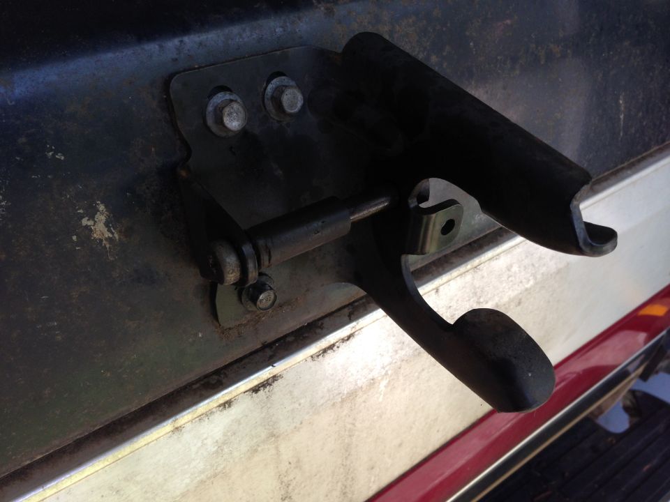 Tailgate latch mechanism on a dark-colored vehicle with a red stripe
