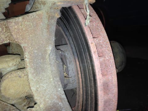 1990 Ford Bronco - Close-up view of a heavily rusted brake rotor and caliper, indicating significant wear and age.