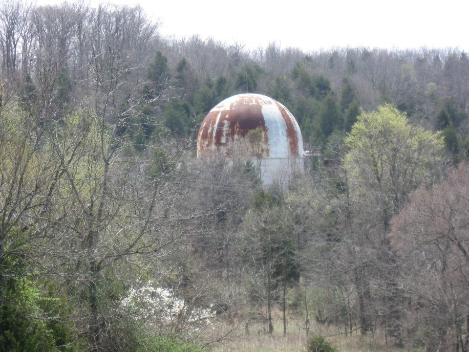 Rusted domed structure partially obscured by trees. White and orange rust patterns visible on dome