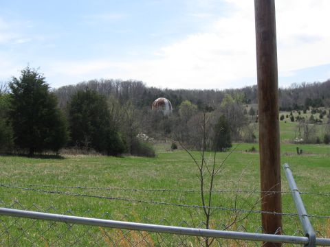 2006 Suzuki DR-Z400S - A distant water tower stands in a grassy field, bordered by trees and a barbed wire fence under a partly cloudy sky.