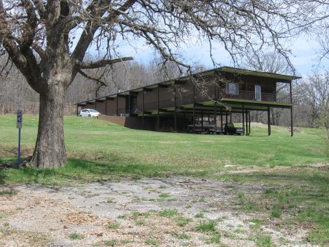 2006 Suzuki DR-Z400S - A house on stilts is surrounded by grass and trees, with vehicles parked in various locations.