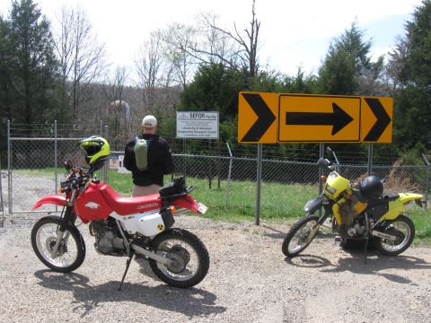 2006 Suzuki DR-Z400S - Two dirt bikes are parked outside a facility with directional signs overhead.