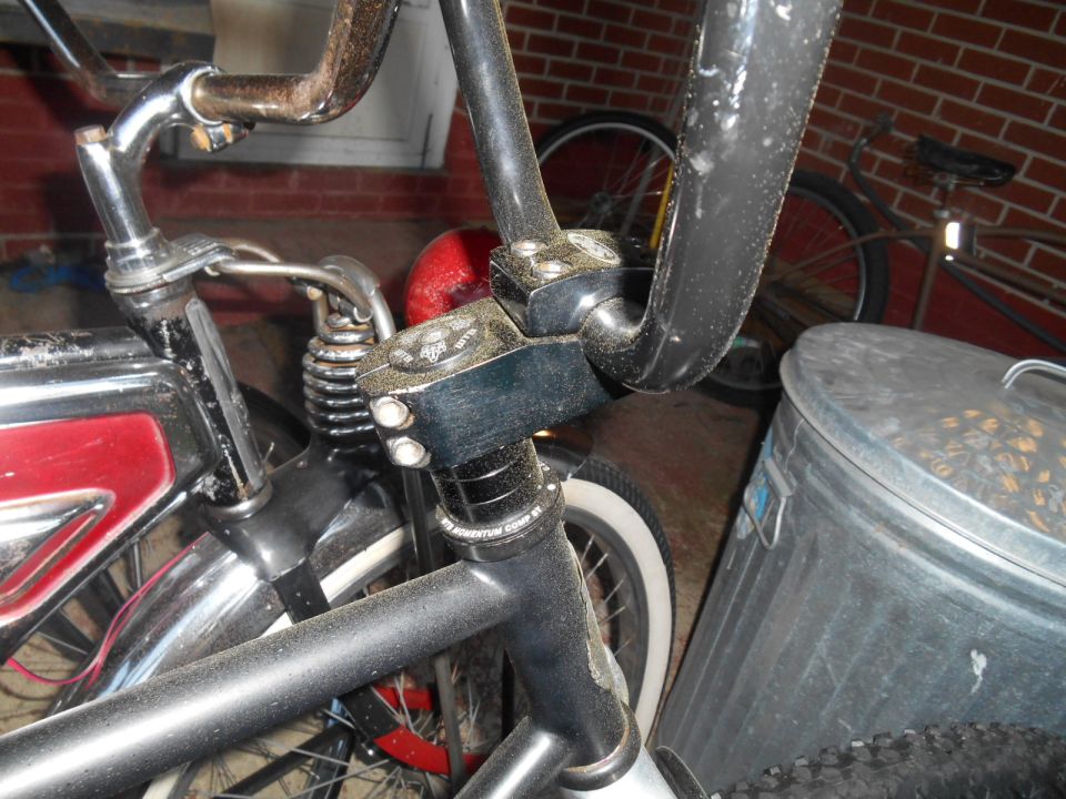 Close-up of bicycle handlebars, stem, and part of the frame. Another bicycle and a trash can are in the background