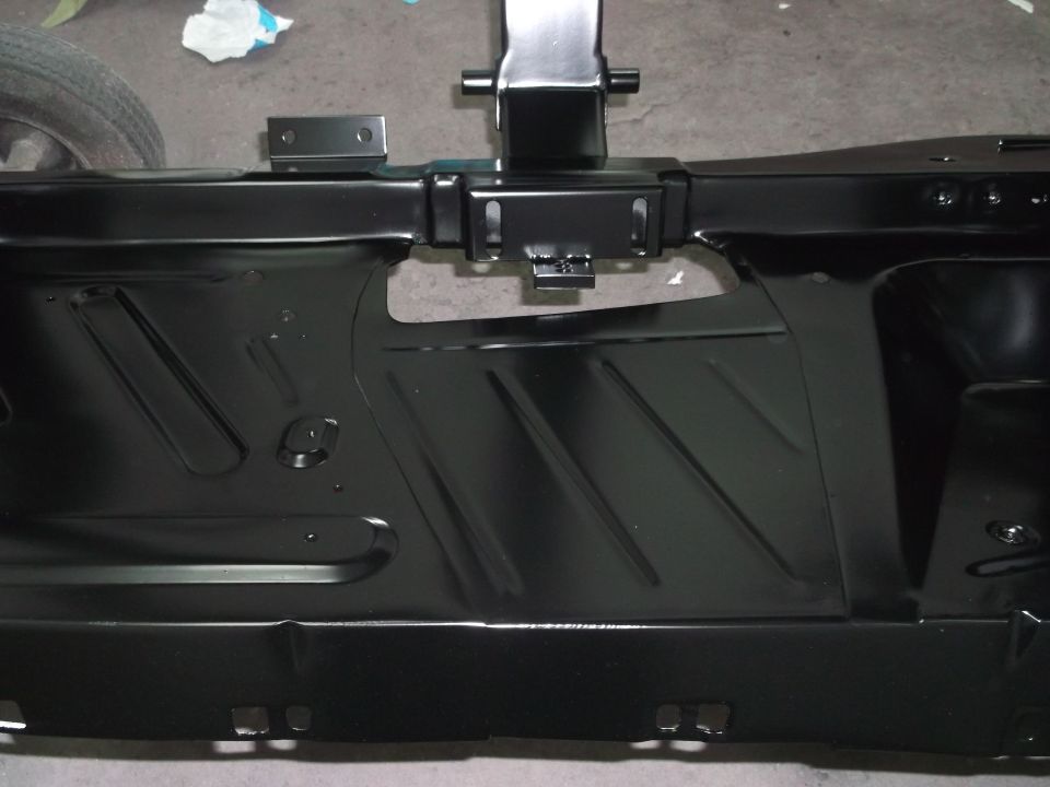 Black metal car frame section with stamped diagonal lines and mounting brackets. A tire is partially visible on the left