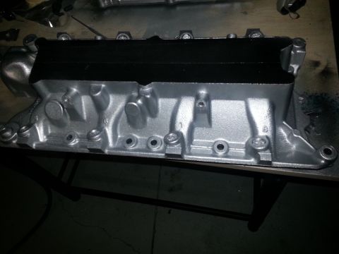 1994 Ford Bronco - Engine intake manifold, painted silver with a black top, sits on a workbench.