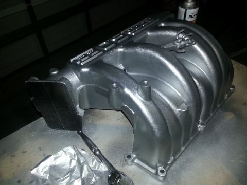 1994 Ford Bronco - A silver intake manifold, likely for a Ford vehicle, sits on a workbench with a socket wrench nearby.