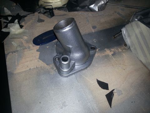 1994 Ford Bronco - A silver thermostat housing sits on a surface with various tools and materials around it.