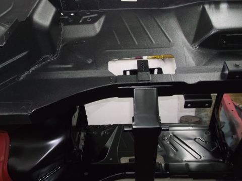 1967 Ford Mustang - Underside view of a car's interior floor pan, showing structural components and a tool resting on a white bracket.