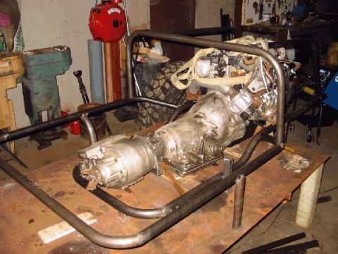 1994 Ford Bronco - Engine and transmission assembly mounted within a custom roll cage frame on a workbench.
