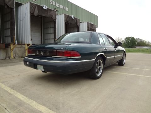 1993 Mercury Grand Marquis - Rear view of a dark green 1993 Mercury Grand Marquis parked in front of a shipping dock.