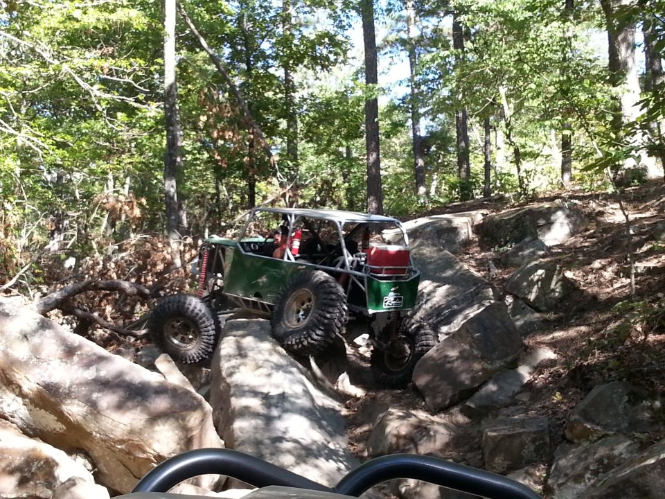 Green off-road buggy with large tires navigating a rocky trail in a forest