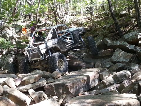 1967 Ford Mustang - A heavily modified off-road buggy navigates a challenging rocky terrain in a wooded area.
