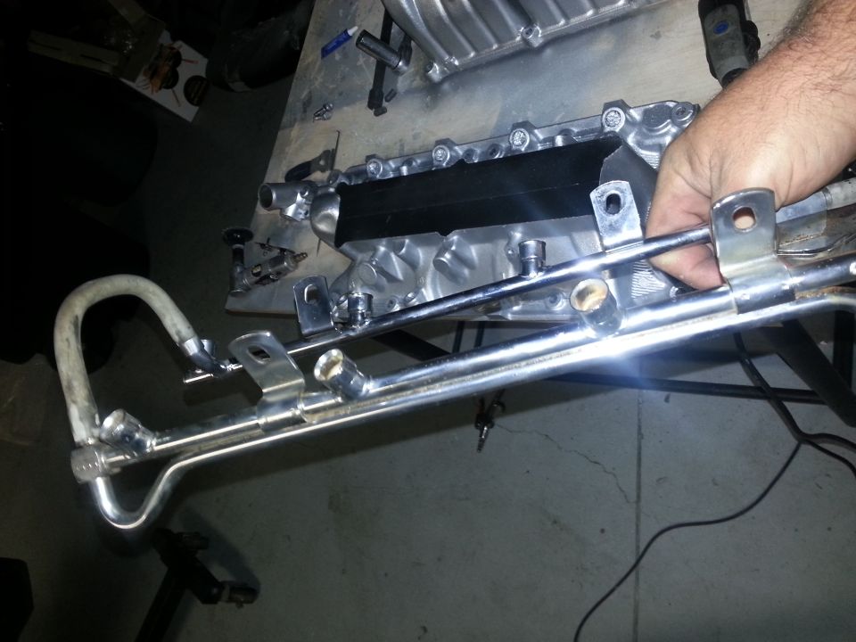 hand holding chrome fuel rail assembly with metal tubing and connectors