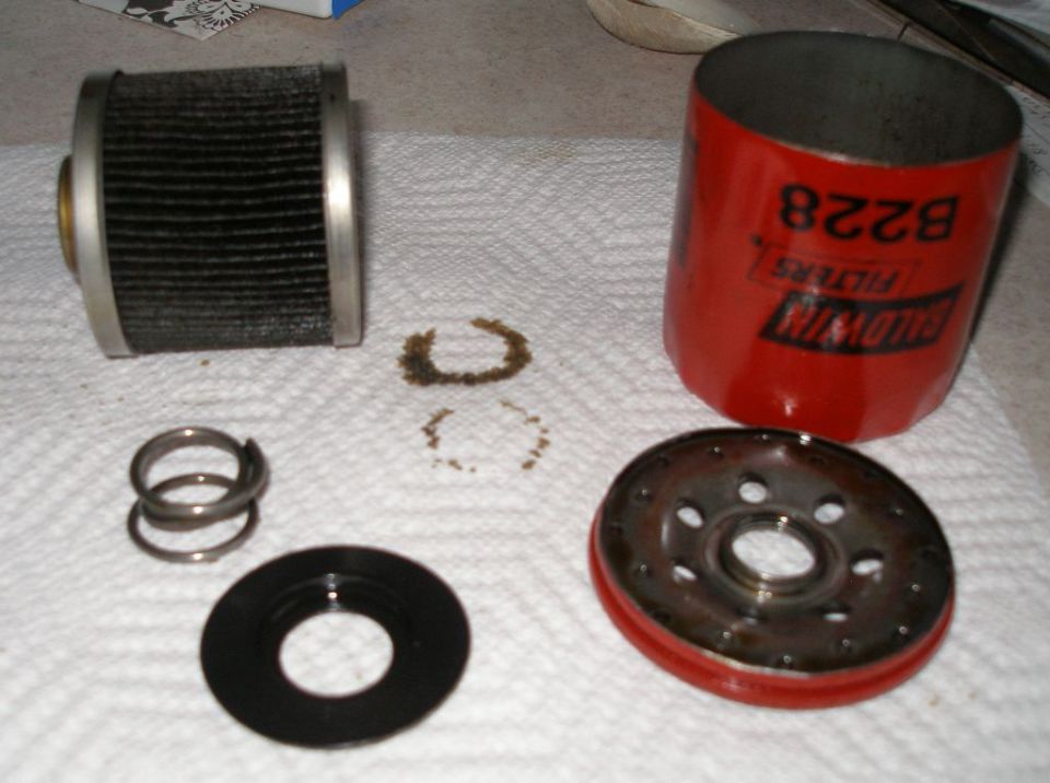 Disassembled oil filter with Baldwin Filters B228 label, spring, and gasket on a white paper towel