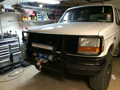 1996 Ford Bronco - Front view of a white Ford Bronco, equipped with a bull bar, winch, and LED light bar, parked in a garage.