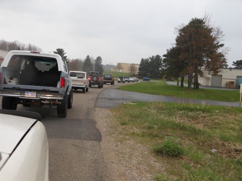 1995 Ford Bronco - A convoy of Ford Broncos, including a 1995 model, travels down a paved road near an industrial building.