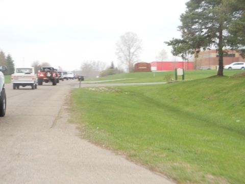 1995 Ford Bronco - A convoy of vehicles, including a tan Ford Bronco, travels down a paved road on an overcast day.