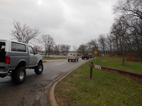 1995 Ford Bronco - A convoy of SUVs drives down a road on an overcast day, with a lifted Bronco in the foreground.