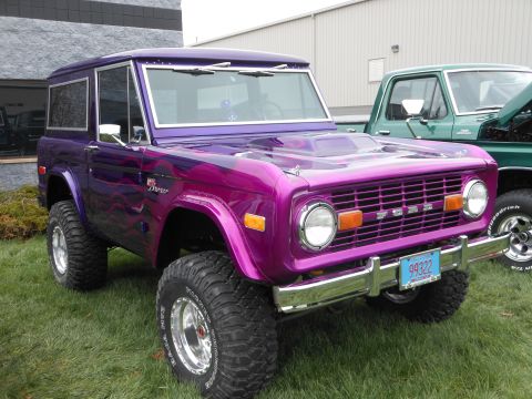 1995 Ford Bronco - This custom Ford Bronco features a vibrant purple paint job with flame graphics and a prominent hood scoop.