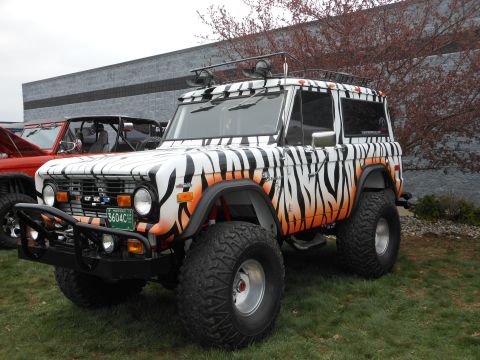 1995 Ford Bronco - This lifted Ford Bronco features a distinctive tiger stripe paint job and orange accents, parked next to another vehicle.