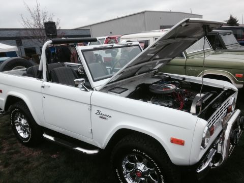 1995 Ford Bronco - White convertible SUV with hood open, revealing the engine. Another SUV is visible behind it.