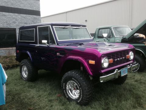 1995 Ford Bronco - A custom purple Ford Bronco is parked next to a green pickup truck.