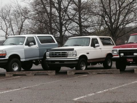 1995 Ford Bronco - Three SUVs, including two Ford Broncos, are parked in a lot. The front Bronco appears to be a 1995 model.