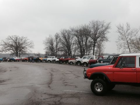 1995 Ford Bronco - A gathering of Ford Broncos parked in a lot, with a red Bronco prominently in the foreground.