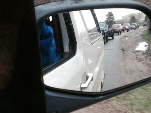 1995 Ford Bronco - Reflection in a side mirror reveals a convoy of vintage SUVs and trucks driving on a rural road.