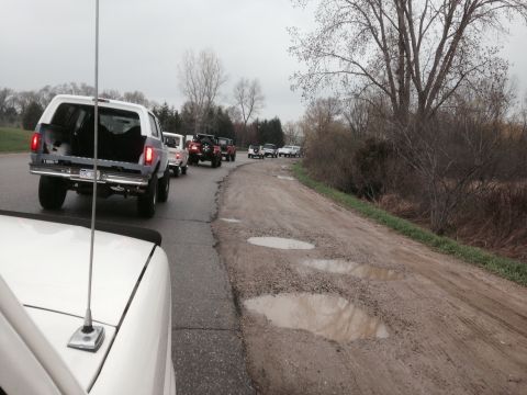 1995 Ford Bronco - A convoy of SUVs, including a white 1995 Ford Bronco, navigates a pothole-ridden dirt road.