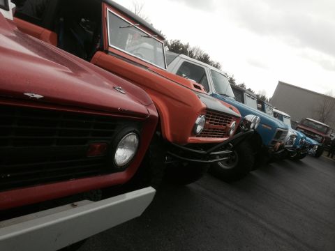 1995 Ford Bronco - A row of classic Ford Broncos, including red, orange, and blue models, parked outdoors.