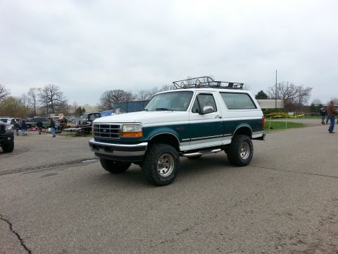 1995 Ford Bronco - A two-tone Ford Bronco is parked in an outdoor lot with other vehicles and people around.