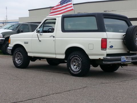 1995 Ford Bronco - White 1995 Ford Bronco with black top and spare tire on back, flying an American flag.