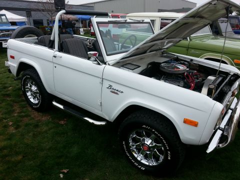 1995 Ford Bronco - White first-gen Ford Bronco on display, hood up to reveal the engine bay.