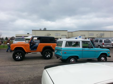 1995 Ford Bronco - Two classic Ford Broncos, an orange lifted model and a blue two-door, are parked together at an outdoor event.