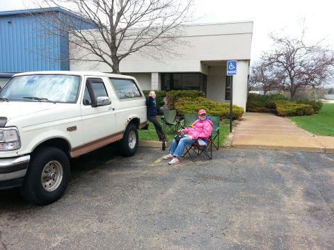 1995 Ford Bronco - Two people relax in lawn chairs next to a white Ford Bronco in a parking lot.