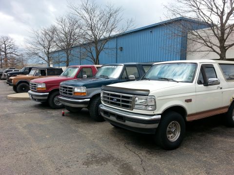 1995 Ford Bronco - Several Ford Broncos are parked in a row outside a blue building.