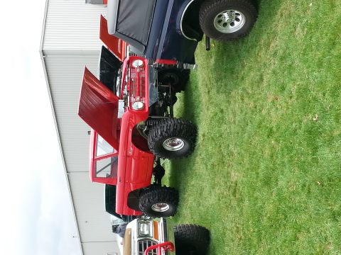 1995 Ford Bronco - Several lifted trucks, including a red first-gen Ford Bronco, are parked on grass with hoods open.