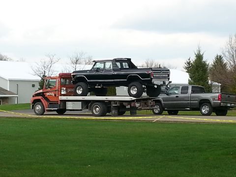 1995 Ford Bronco - A black lifted pickup truck is transported on a flatbed tow truck, with another pickup truck visible behind it.