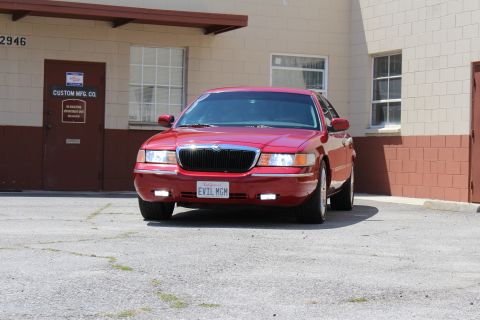 2002 Mercury Grand Marquis - A red 2002 Mercury Grand Marquis is parked in front of a building, displaying a custom license plate.