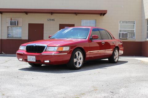2002 Mercury Grand Marquis - The red sedan has a custom license plate that reads 'EVIL MGM'.